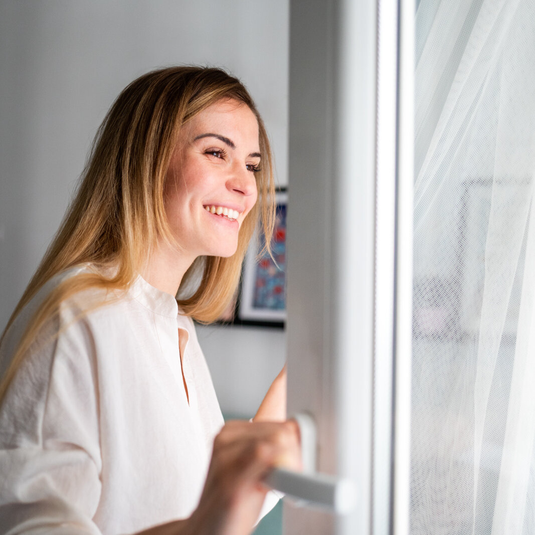 Beautiful smiling young woman opening window at the morning, fresh air, 
