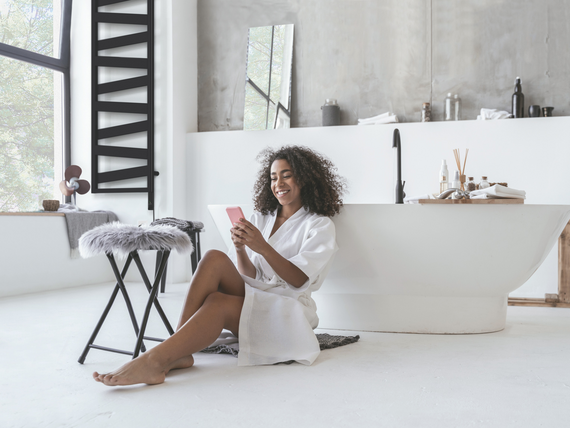 Smiling woman sitting in the bathroom on the floor with a smartphone in her hands